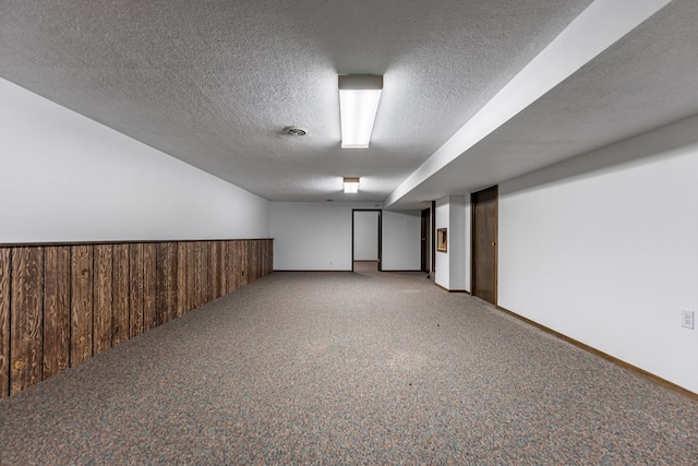 finished below grade area with wooden walls, visible vents, a wainscoted wall, a textured ceiling, and carpet flooring