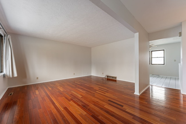 empty room with hardwood / wood-style floors, a ceiling fan, baseboards, visible vents, and a textured ceiling