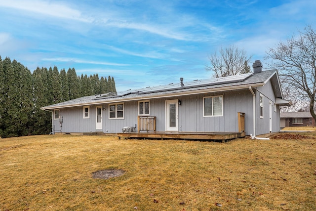 back of house featuring a yard, solar panels, a wooden deck, and a chimney