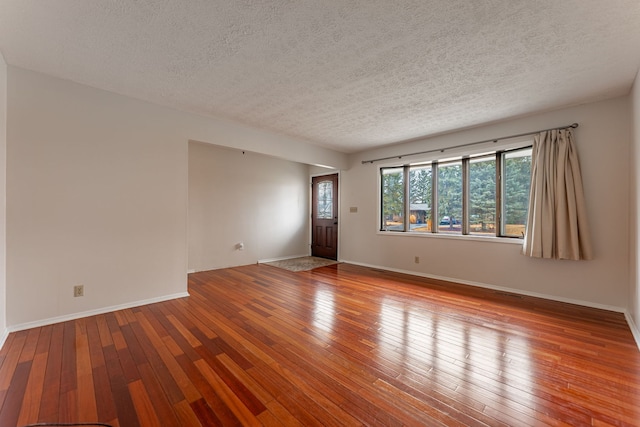 empty room featuring hardwood / wood-style flooring, visible vents, baseboards, and a textured ceiling