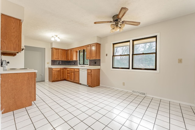 kitchen with a ceiling fan, light countertops, dishwasher, brown cabinets, and backsplash