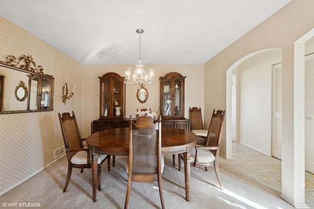 dining room featuring visible vents, wallpapered walls, arched walkways, light colored carpet, and a chandelier