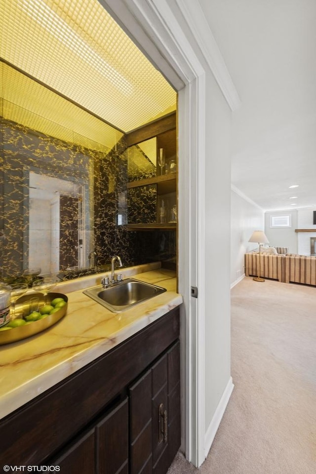 interior space with baseboards, light colored carpet, ornamental molding, wet bar, and a sink