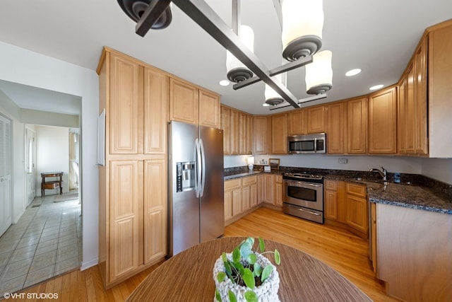 kitchen featuring dark stone counters, recessed lighting, light wood-style floors, stainless steel appliances, and a sink