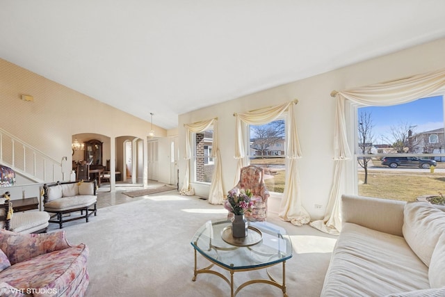 carpeted living area featuring arched walkways, stairs, and vaulted ceiling