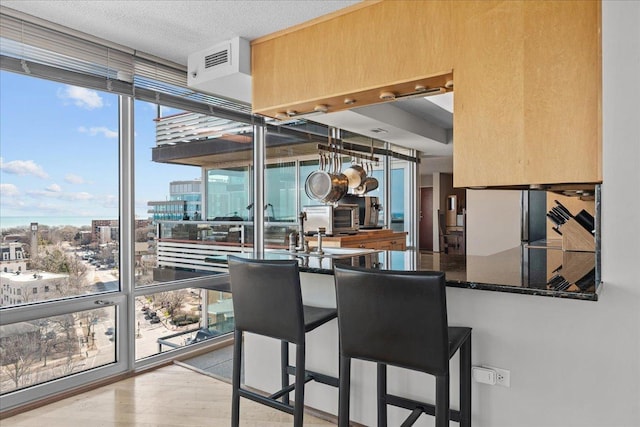 kitchen with wood finished floors, dark stone counters, floor to ceiling windows, a textured ceiling, and a view of city