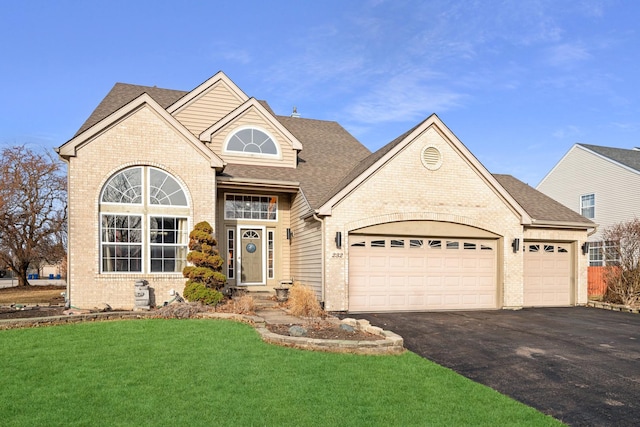 traditional-style house with a front yard, driveway, roof with shingles, a garage, and brick siding