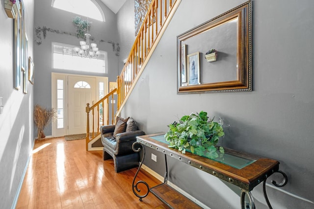 foyer featuring stairway, baseboards, hardwood / wood-style flooring, a towering ceiling, and a chandelier