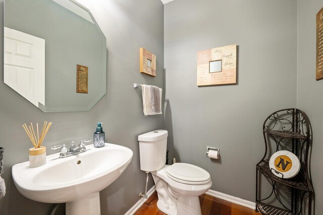 half bathroom with wood finished floors, toilet, baseboards, and a sink