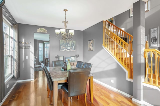 dining space featuring visible vents, baseboards, a chandelier, stairs, and wood finished floors