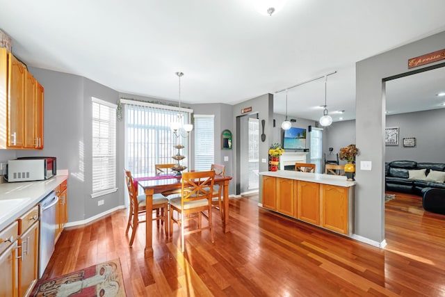 kitchen featuring white microwave, light wood finished floors, dishwasher, pendant lighting, and light countertops