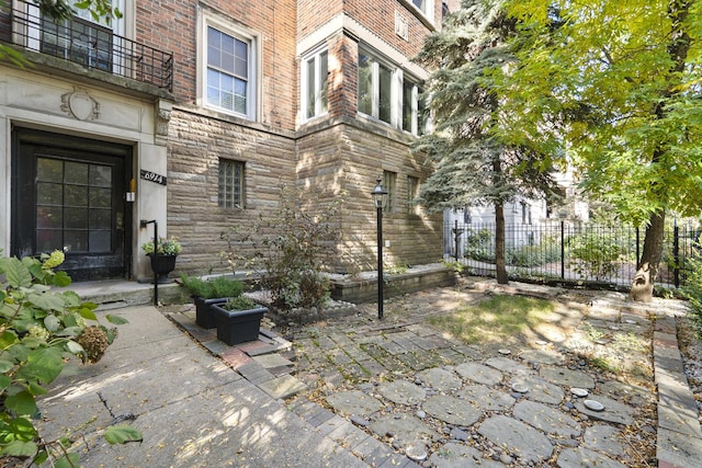 entrance to property featuring brick siding, stone siding, and fence