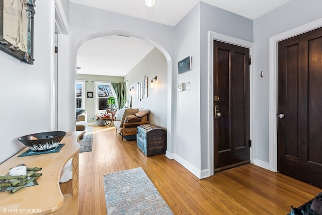 foyer with baseboards, arched walkways, and wood-type flooring