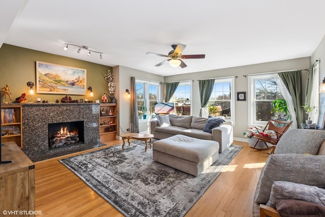 living room with a ceiling fan, baseboards, light wood-type flooring, and a premium fireplace