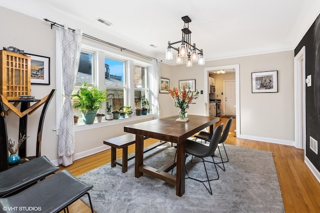 dining space with visible vents, baseboards, light wood-style floors, crown molding, and a notable chandelier