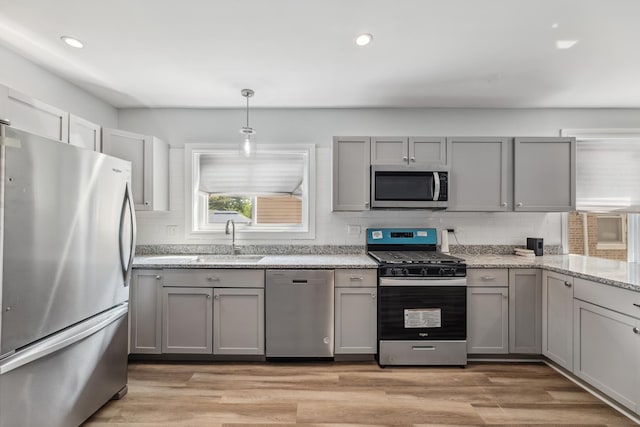 kitchen featuring a sink, gray cabinetry, appliances with stainless steel finishes, light wood-type flooring, and backsplash