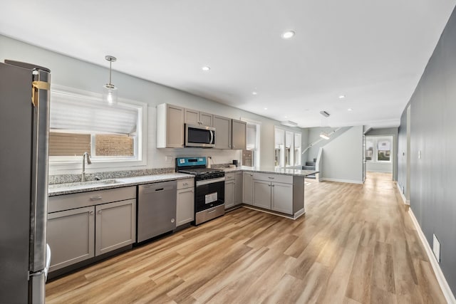 kitchen featuring a peninsula, gray cabinets, a sink, light wood-style floors, and appliances with stainless steel finishes