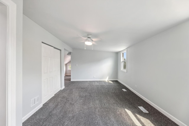 spare room featuring a wealth of natural light, visible vents, a ceiling fan, and dark colored carpet