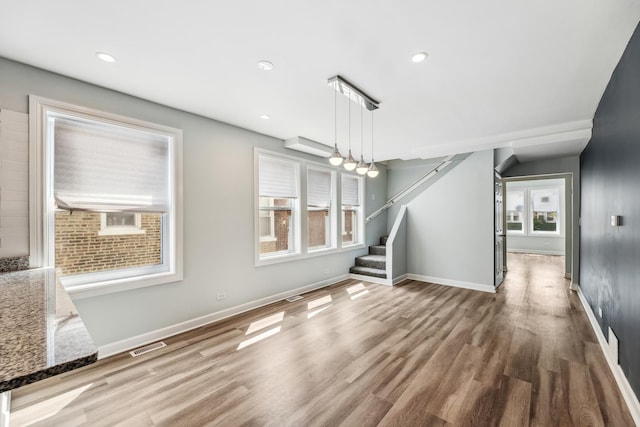 unfurnished dining area with visible vents, baseboards, wood finished floors, and stairs