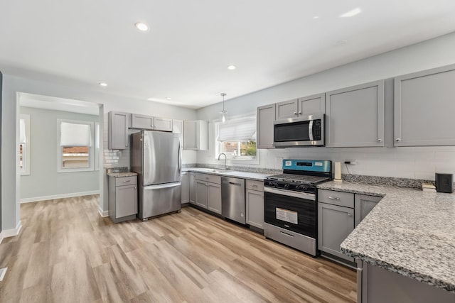 kitchen with light wood-type flooring, a sink, gray cabinetry, stainless steel appliances, and tasteful backsplash