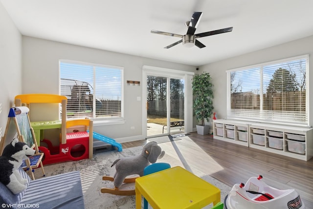 game room featuring a healthy amount of sunlight, ceiling fan, baseboards, and wood finished floors