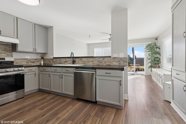 kitchen featuring under cabinet range hood, dark countertops, appliances with stainless steel finishes, and gray cabinetry