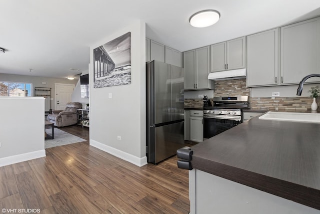 kitchen with gray cabinets, a sink, under cabinet range hood, dark countertops, and appliances with stainless steel finishes