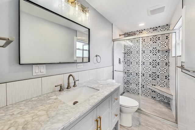 bathroom with a wainscoted wall, visible vents, toilet, a shower stall, and vanity