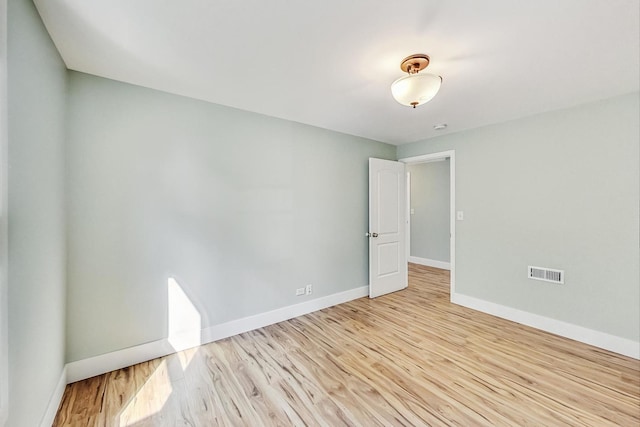 empty room with light wood-style floors, visible vents, and baseboards