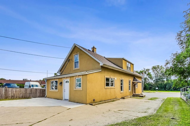 view of side of property featuring a patio area, fence, a chimney, and stucco siding