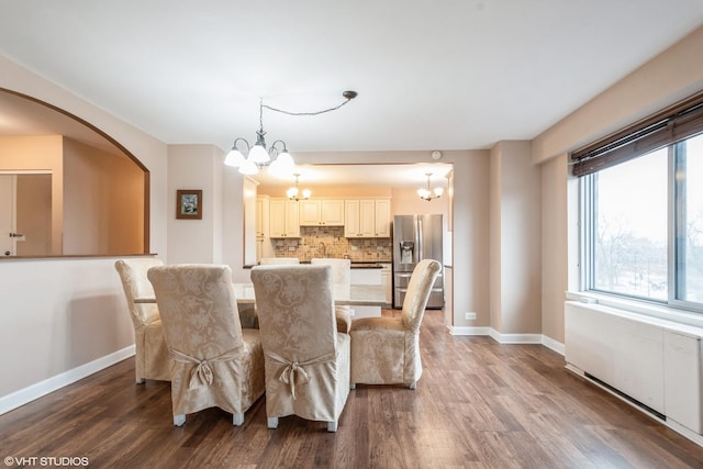 dining space featuring a chandelier, arched walkways, dark wood-type flooring, and baseboards