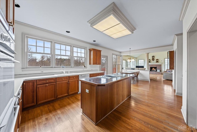 kitchen featuring open floor plan, a kitchen island, a brick fireplace, stainless steel stovetop, and brown cabinetry