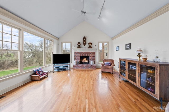 living area featuring light wood-style floors, track lighting, a ceiling fan, a brick fireplace, and baseboards
