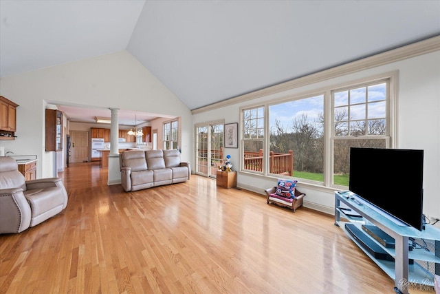 living area featuring high vaulted ceiling, light wood-style floors, ornate columns, and baseboards