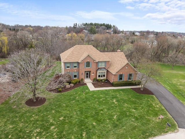 traditional home with brick siding, a chimney, a front lawn, and aphalt driveway