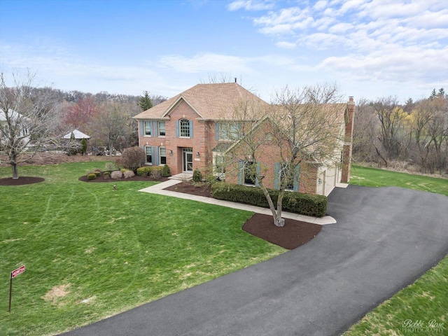 view of front facade featuring brick siding, driveway, a chimney, and a front lawn
