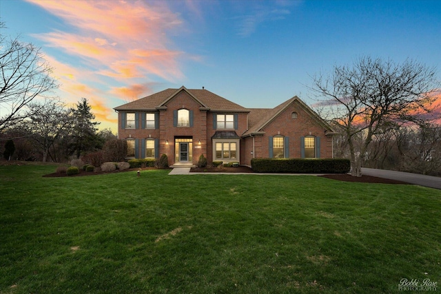 view of front of home with a shingled roof, a front yard, and brick siding