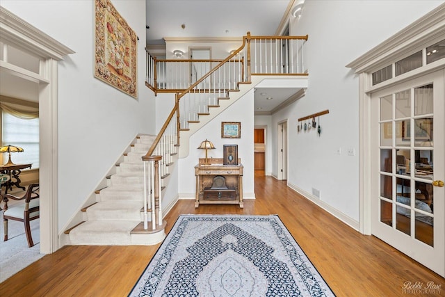 stairs featuring a towering ceiling, baseboards, crown molding, and wood finished floors