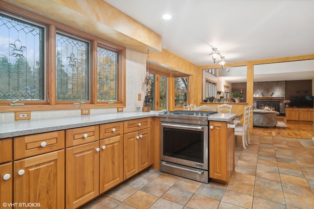 kitchen featuring tasteful backsplash, stainless steel range with gas cooktop, a peninsula, a fireplace, and light stone countertops