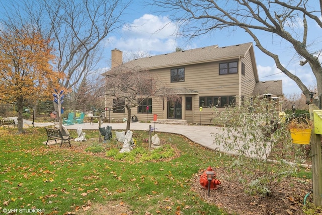 back of property featuring entry steps, a lawn, a chimney, driveway, and a patio