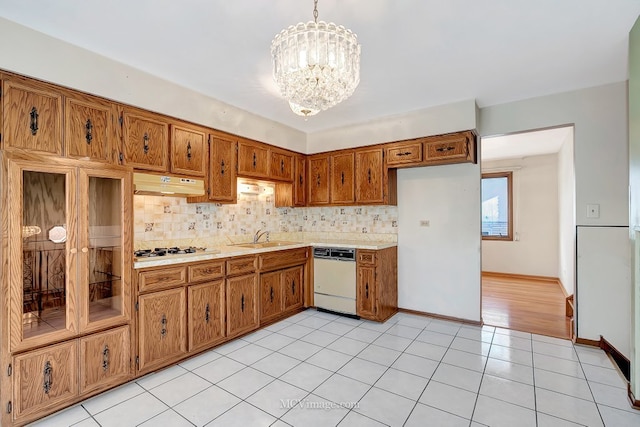 kitchen featuring white appliances, brown cabinetry, a sink, decorative backsplash, and a chandelier