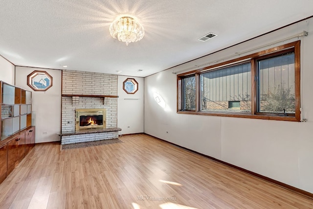 unfurnished living room with visible vents, a textured ceiling, wood finished floors, a fireplace, and baseboards