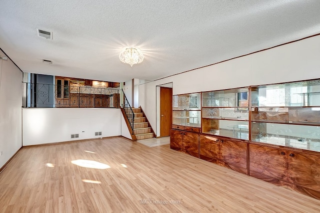 empty room with stairway, wood finished floors, visible vents, and a chandelier