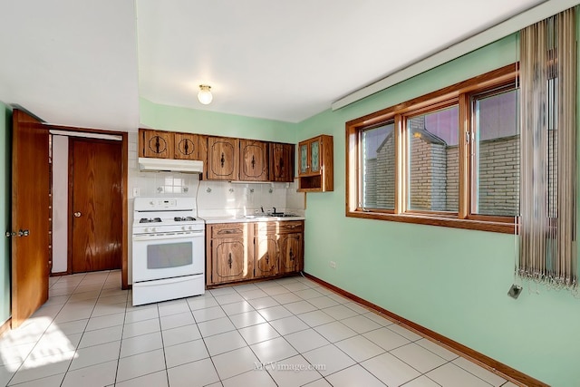 kitchen with baseboards, gas range gas stove, decorative backsplash, light countertops, and under cabinet range hood