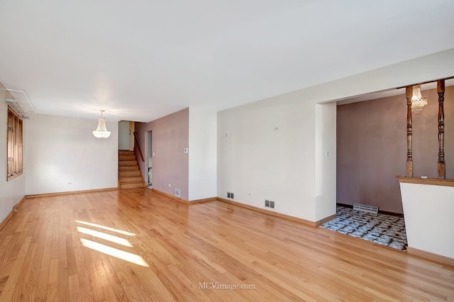 empty room featuring light wood-type flooring, visible vents, baseboards, and stairway