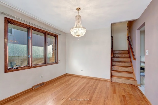 spare room featuring visible vents, stairway, light wood-style floors, baseboards, and a chandelier