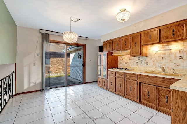 kitchen with under cabinet range hood, an inviting chandelier, brown cabinetry, and a sink