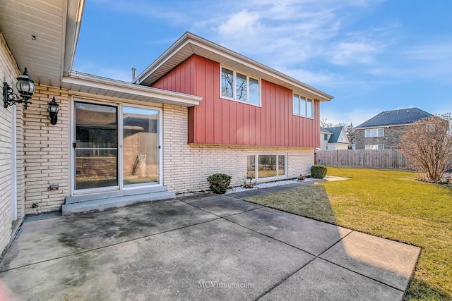 back of house with a lawn, fence, board and batten siding, brick siding, and a patio area