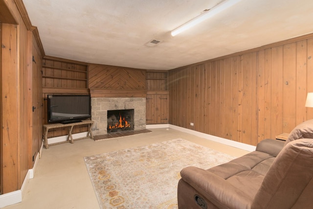 living room with wooden walls, built in shelves, baseboards, visible vents, and a stone fireplace