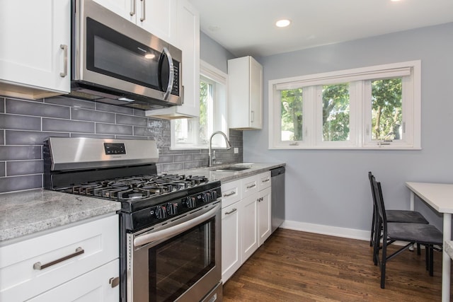 kitchen with a sink, stainless steel appliances, decorative backsplash, baseboards, and light stone countertops